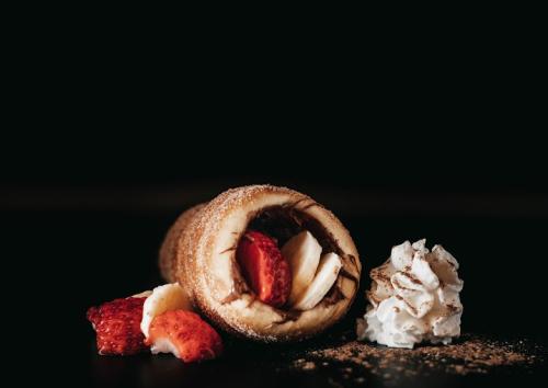 A dessert cone filled with chocolate, strawberries, and bananas, accompanied by a dollop of whipped cream.