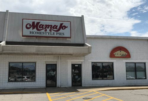 Exterior of Mama Jo's Homestyle Pies shop, featuring a sign and large windows under a partly cloudy sky.