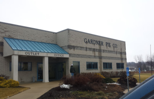 Exterior of Gardner Pie Co. building with a blue roof, featuring an outlet office and surrounding landscaping.