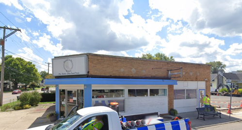 A brick building with a blue awning and sign, featuring a truck parked in front and construction equipment nearby.