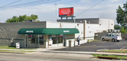 A storefront with a green awning, parking lot, and a billboard advertising an event on August 21.