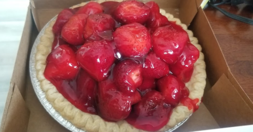 A strawberry pie topped with glossy red strawberries in a shiny glaze, sitting in a pie box.