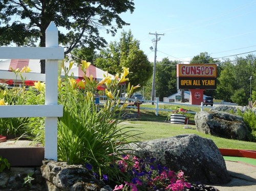 A colorful outdoor scene at Funspot, featuring flowers, rocks, and a sign that reads "OPEN ALL YEAR."