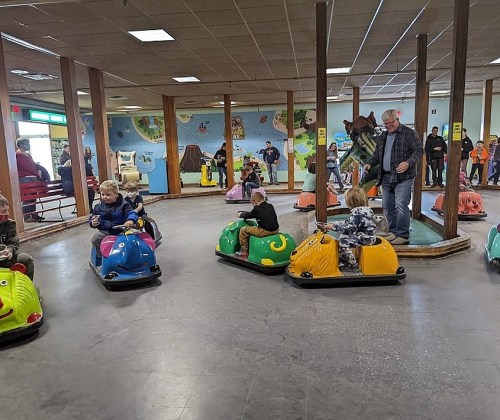 Children and adults enjoy bumper cars in a lively indoor amusement area with colorful vehicles and playful decor.