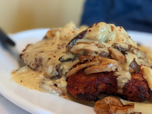 A plate of crispy chicken topped with creamy mushroom sauce and served with a side of pasta.