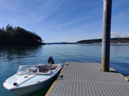 A small boat docked at a wooden pier, with calm water and a clear blue sky in the background.