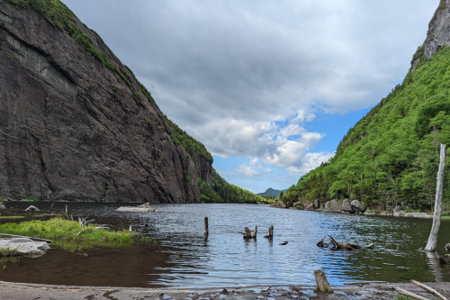 A serene lake surrounded by steep cliffs and lush greenery under a partly cloudy sky.