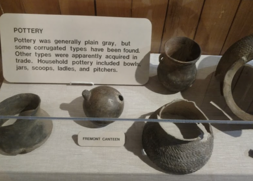 Display of various gray pottery pieces, including bowls and jars, with an informational sign about their history.