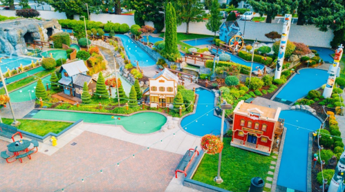 Aerial view of a colorful mini-golf course with themed structures, water features, and lush landscaping.