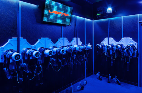 A dimly lit room with blue lighting featuring multiple laser tag headsets mounted on the wall and a screen displaying "Laser Tag."