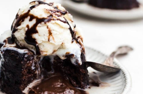 A decadent chocolate dessert with a scoop of vanilla ice cream and chocolate sauce, partially eaten on a plate.