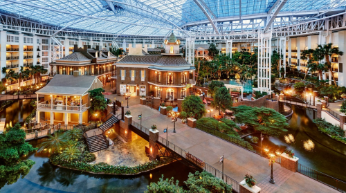 A spacious indoor garden with tropical plants, water features, and a glass roof, creating a serene resort atmosphere.