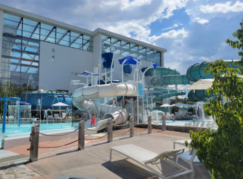 A water park featuring colorful slides, a pool area, and lounge chairs under a blue sky with scattered clouds.
