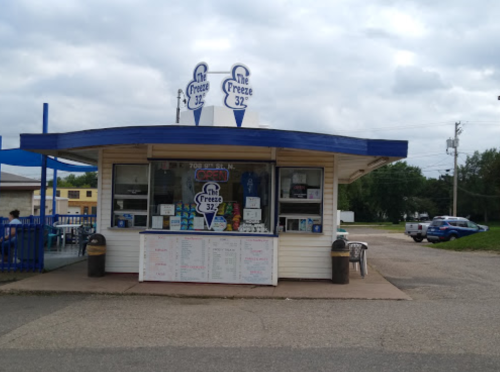 A small ice cream stand with a blue roof, featuring a sign that says "Freeze 32" and outdoor seating.