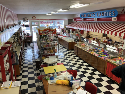 A colorful candy shop interior with checkered floors, display cases, and a seating area. Brightly decorated for the holidays.