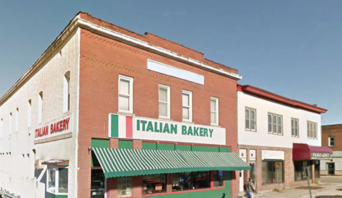 A red brick building with a green awning, featuring a sign that reads "Italian Bakery" in bold letters.