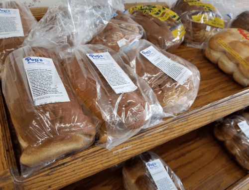 Loaves of bread in clear packaging displayed on a wooden shelf, labeled with product information.