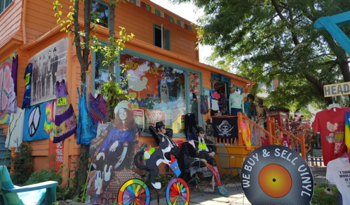 Colorful storefront with eclectic decorations, including tie-dye shirts, art, and a sign that says "We Buy & Sell Vinyl."