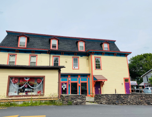 A colorful thrift shop building with a stone wall, featuring large windows and a vibrant exterior.