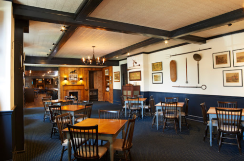 Cozy dining area with wooden tables, chairs, and rustic decor, featuring a fireplace and framed artwork on the walls.
