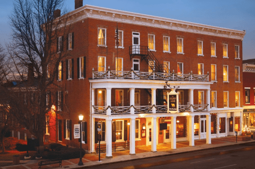 Historic brick hotel with illuminated windows, a balcony, and a welcoming entrance at dusk.