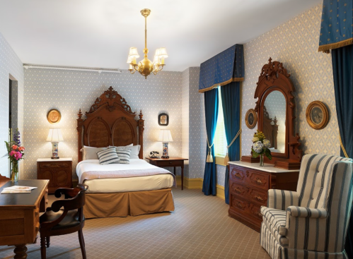 A cozy, elegantly decorated bedroom featuring a wooden bed, vintage furniture, and soft blue accents.