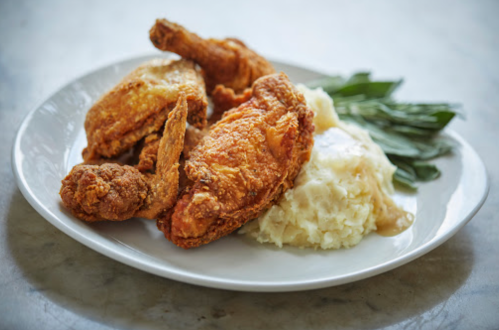 A plate of crispy fried chicken with creamy mashed potatoes and green garnish.