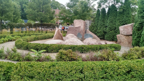 A landscaped garden featuring large rocks, greenery, and a winding path, with people in the background.