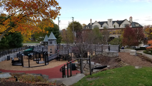 A playground with a castle structure, surrounded by trees with autumn leaves and a view of nearby buildings.