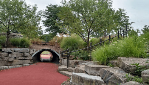 A winding path leads through a park with stone features, greenery, and a tunnel under a grassy area.