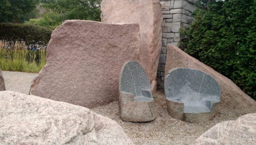 Two stone chairs carved from large rocks, surrounded by smaller boulders in a landscaped area.