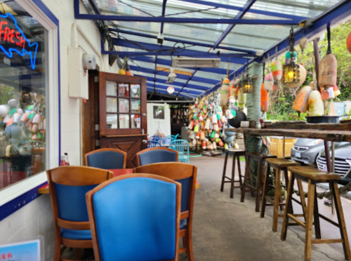 A cozy outdoor dining area with colorful decor, wooden tables, and hanging lanterns, surrounded by greenery.