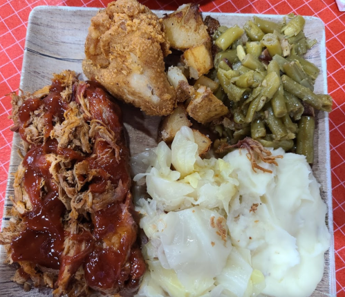 A plate of food featuring pulled pork with barbecue sauce, fried chicken, potatoes, green beans, and mashed cabbage.