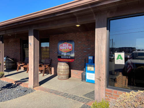 Exterior view of Ole South restaurant featuring a sign, wooden seating, and a barrel near the entrance.