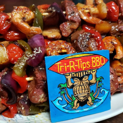 Colorful skewers of shrimp, beef, and vegetables with a "Tri-R-Tips BBQ" sign in the foreground.