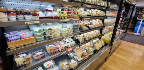 A display of various pre-packaged salads, fruits, snacks, and desserts in a grocery store.
