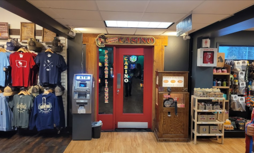 Entrance to a casino with a red door, surrounded by merchandise displays and an ATM on the left.