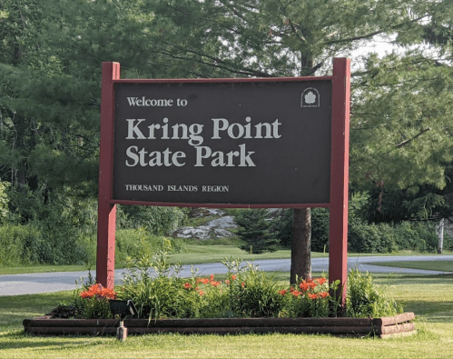 Sign welcoming visitors to Kring Point State Park in the Thousand Islands Region, surrounded by greenery and flowers.