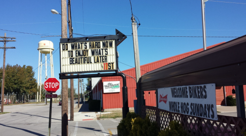 A sign reads, "Do what's hard now to enjoy what's beautiful later," near a stop sign and a water tower.