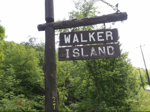 Wooden sign reading "Walker Island" hanging from a post, surrounded by lush greenery.
