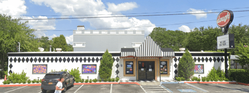 A colorful restaurant with a striped roof and diamond-patterned exterior, surrounded by trees and parked cars.