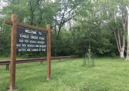 Sign welcoming visitors to Eagle Creek Park, with parking fees listed, surrounded by greenery and trees.