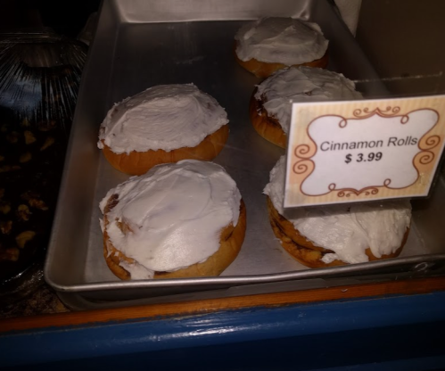 A tray of cinnamon rolls with white icing, priced at $3.99, displayed in a bakery case.