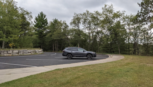 A black SUV parked on a winding road surrounded by trees and grassy areas under a cloudy sky.