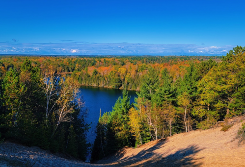 A panoramic view of a serene lake surrounded by vibrant autumn foliage and clear blue skies.