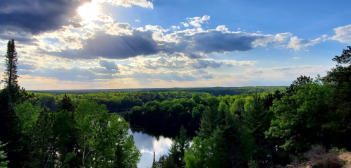 A scenic view of a lush green landscape with a river, under a partly cloudy sky with sunlight streaming through.