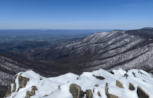 Snow-covered mountain peaks with a clear blue sky and a panoramic view of the valley below.