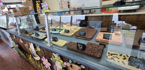 A display case filled with various colorful fudge flavors, each labeled with small black signs.