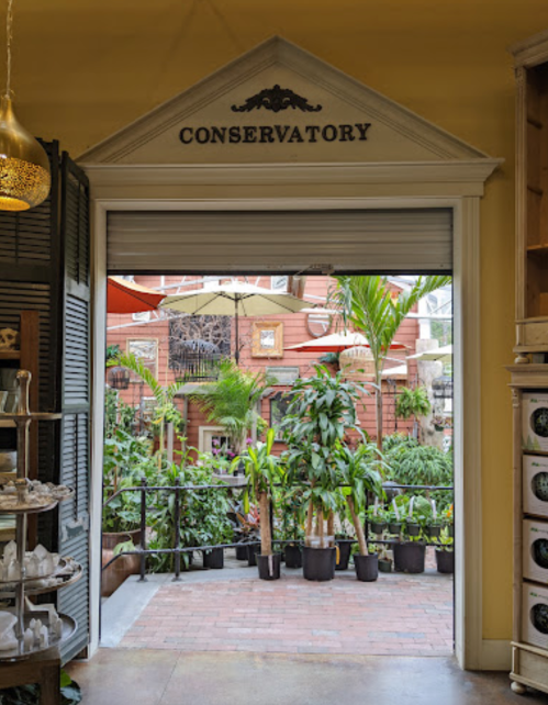 View of a conservatory entrance with lush greenery and potted plants visible through an open doorway.