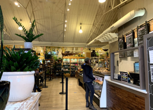 A cozy market interior with shelves of products, a counter, and a customer browsing. Green plants add a natural touch.